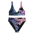Model wearing a high-waisted pastel goth bikini set featuring a black bat and spiderweb print over an ombré pink and purple background. The two-piece swimsuit includes a scoop neck top and high-rise bottoms, styled outdoors in bright festival and poolside settings. Made of recycled fabric, soft, stretchy, and UV resistant. Available in XS to 3X. Aesthetic is gothic, spooky cute, and Y2K inspired.